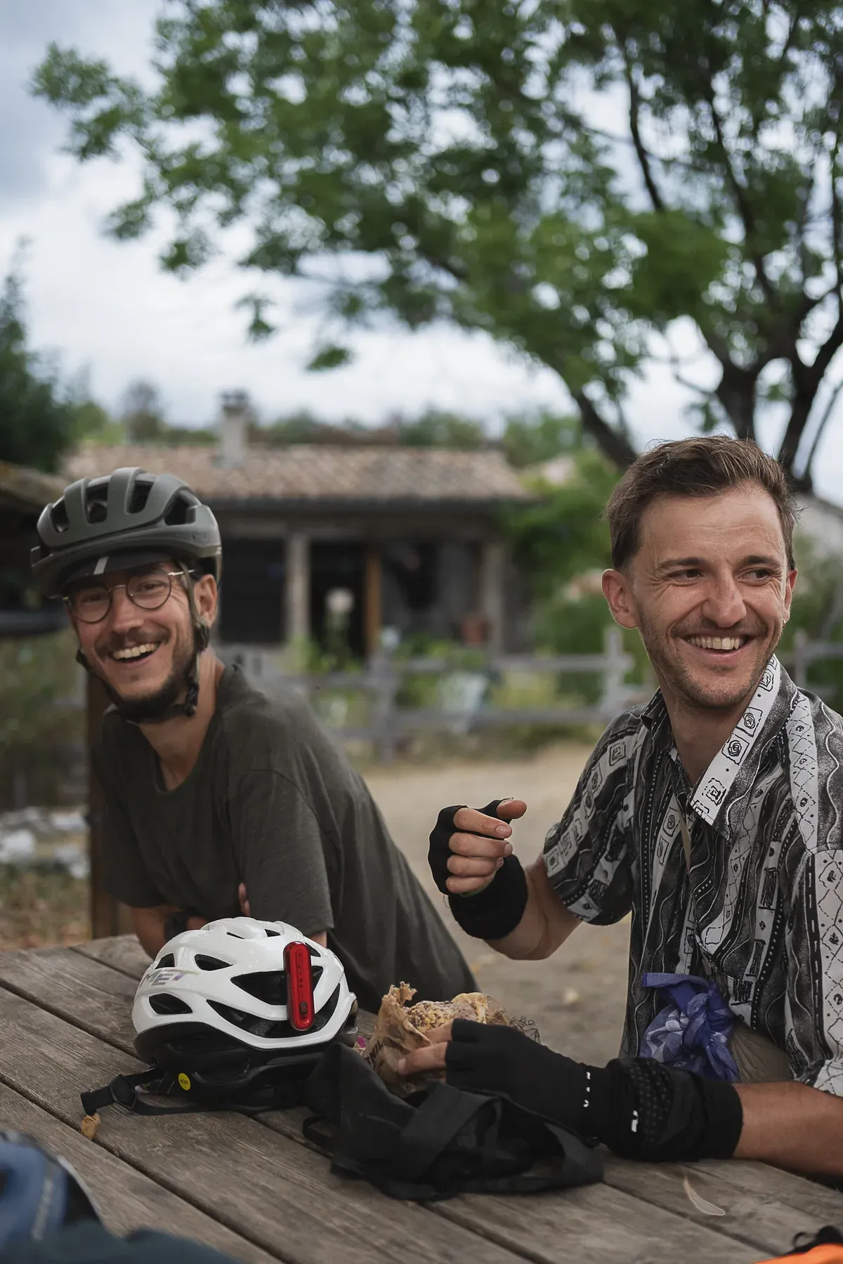 Deux cyclotouristes attablés chez leur hôte, casques posés sur la table